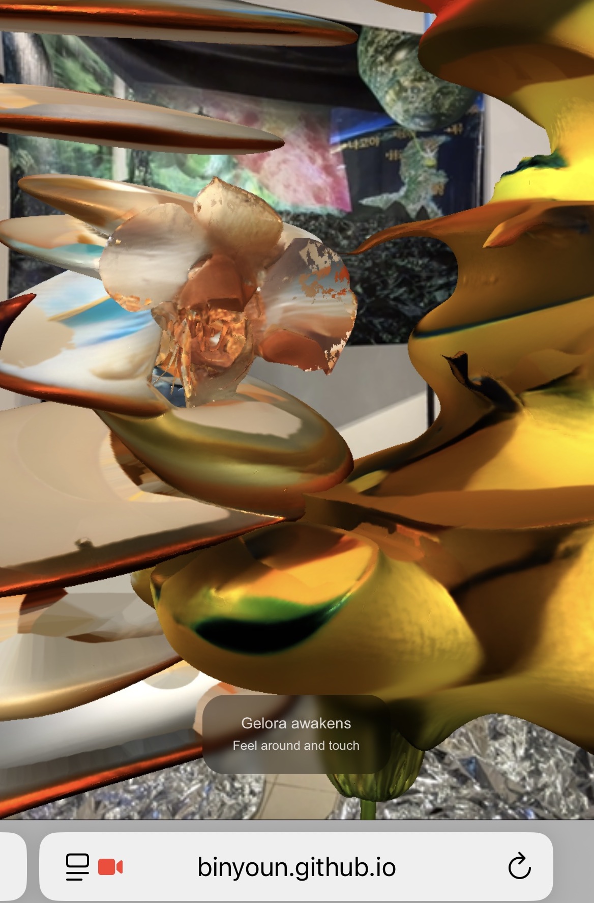 Augmented reality view of a Gelora creature: a preserved, scanned flower at the center surrounded by glossy gold, petal-like digital forms, with on-screen text reading 'Gelora awakens, feel around and touch.'