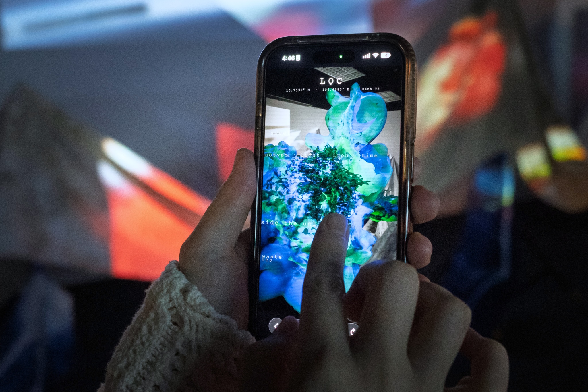 A visitor holds up a phone at the Tẻ Canal installation, the screen showing the Lọc WebAR scene rendered over the site: GPS coordinates and the title LỌC overlaid on a blue and green sculptural form made of filtered debris.